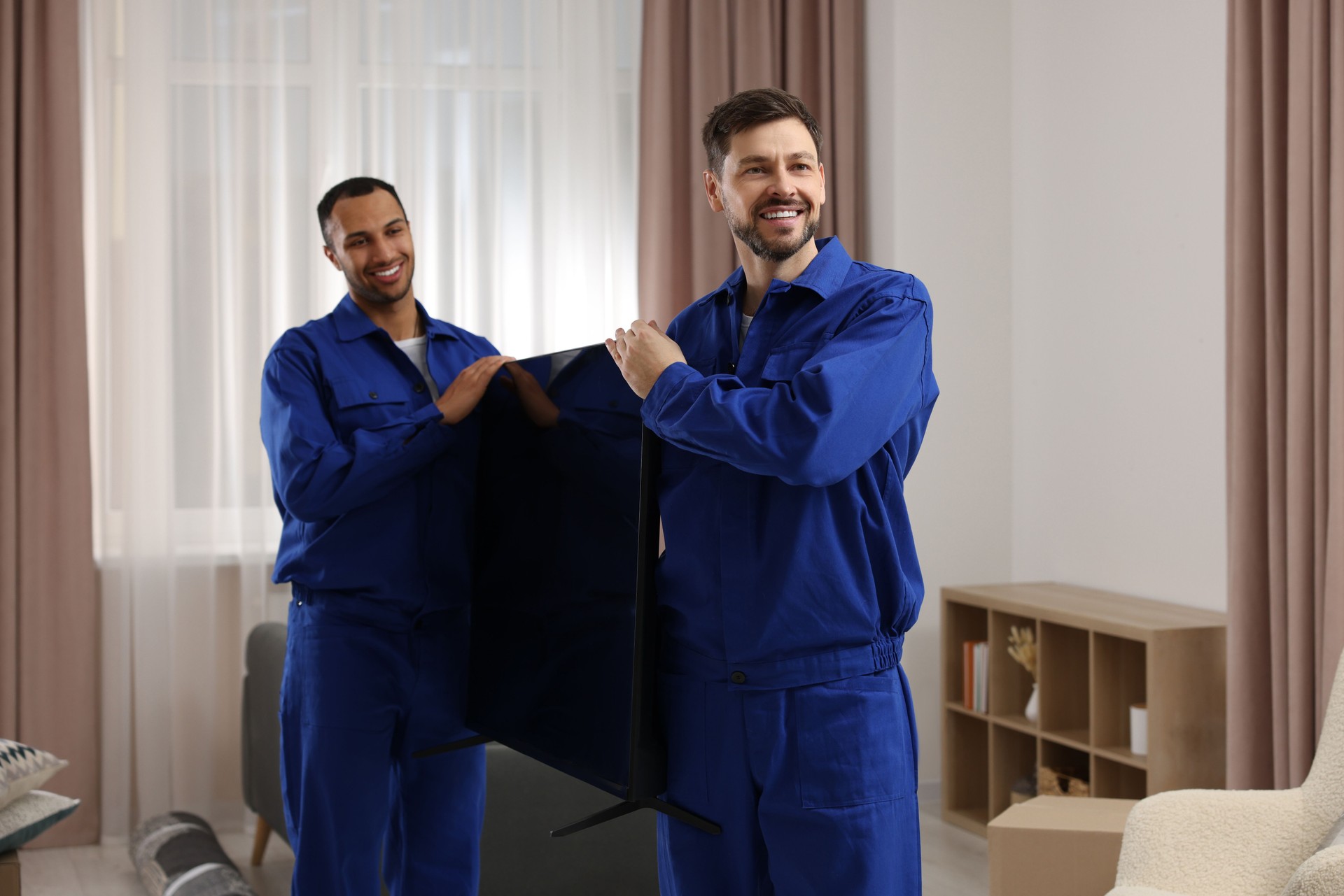 Male movers carrying plasma TV in new house